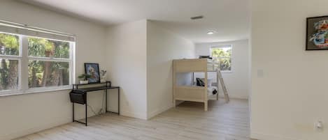 Een kamer met een stapelbed, een bureau met een computer en een raam met jaloezieën.