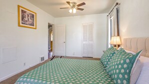 A bedroom with a bed, a ceiling fan, a door, and a window with curtains. - Near Riverwalk & Lake Adventures! Pueblo Home (Pueblo)