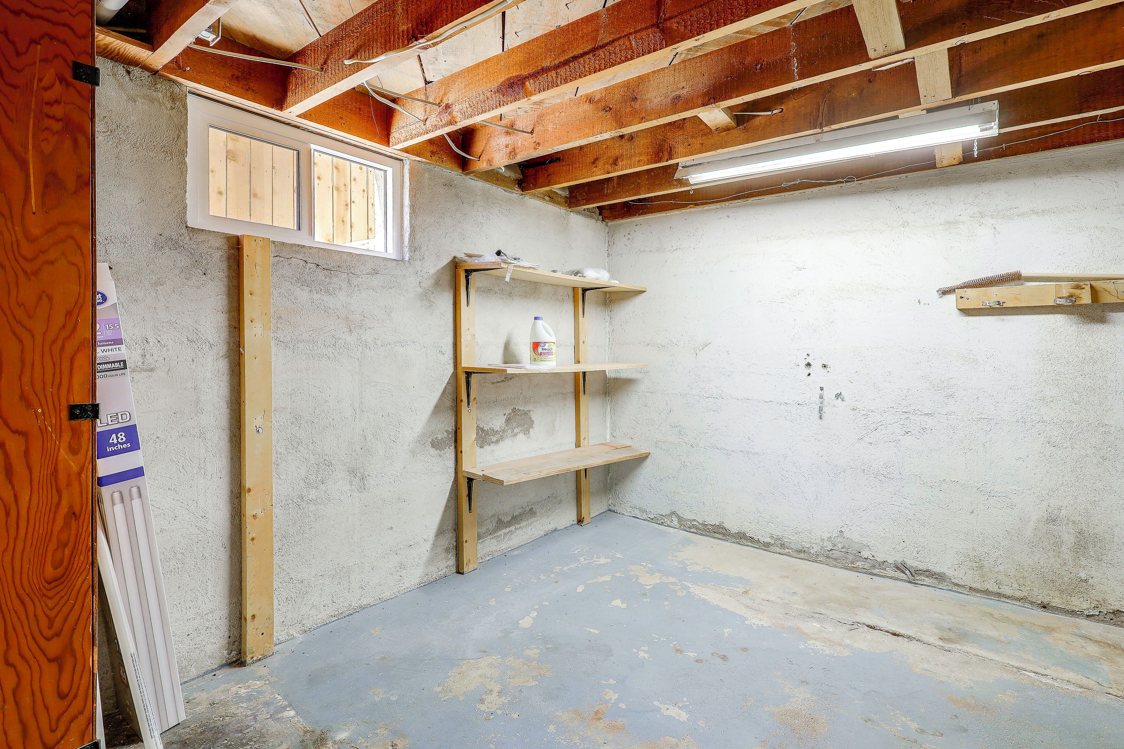 A room with exposed wooden beams, a concrete floor, and a shelf unit with cleaning supplies.
