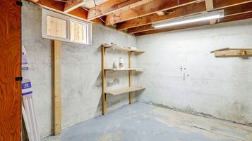 A room with exposed wooden beams, a concrete floor, and a shelf unit with cleaning supplies.