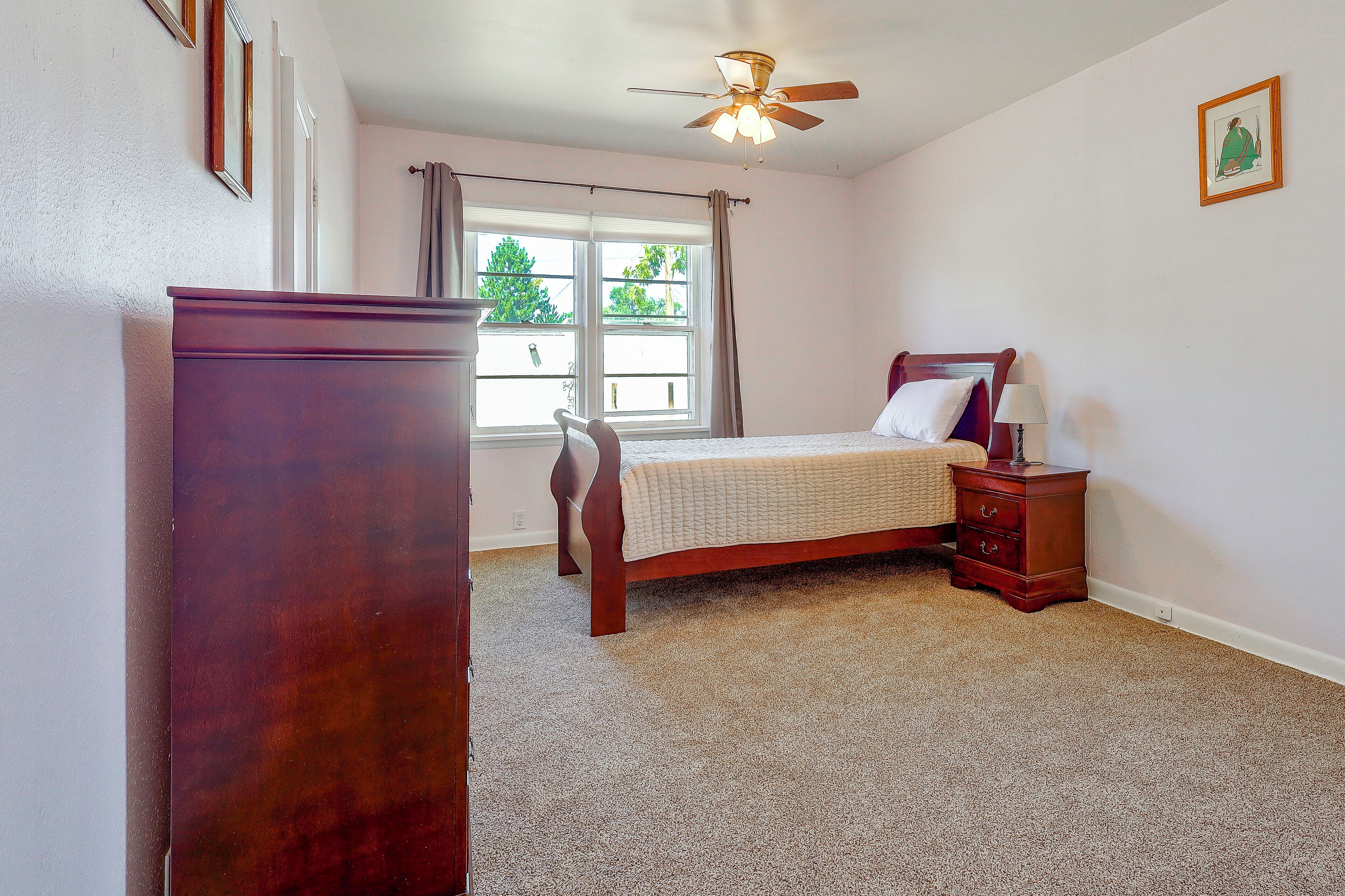 A bedroom with a bed, a nightstand, a dresser, a ceiling fan, and a window with curtains.