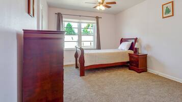 A bedroom with a bed, a nightstand, a dresser, a ceiling fan, and a window with curtains.