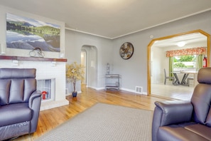 Una sala de estar con chimenea, sillones de cuero, un reloj y vistas al área del comedor.