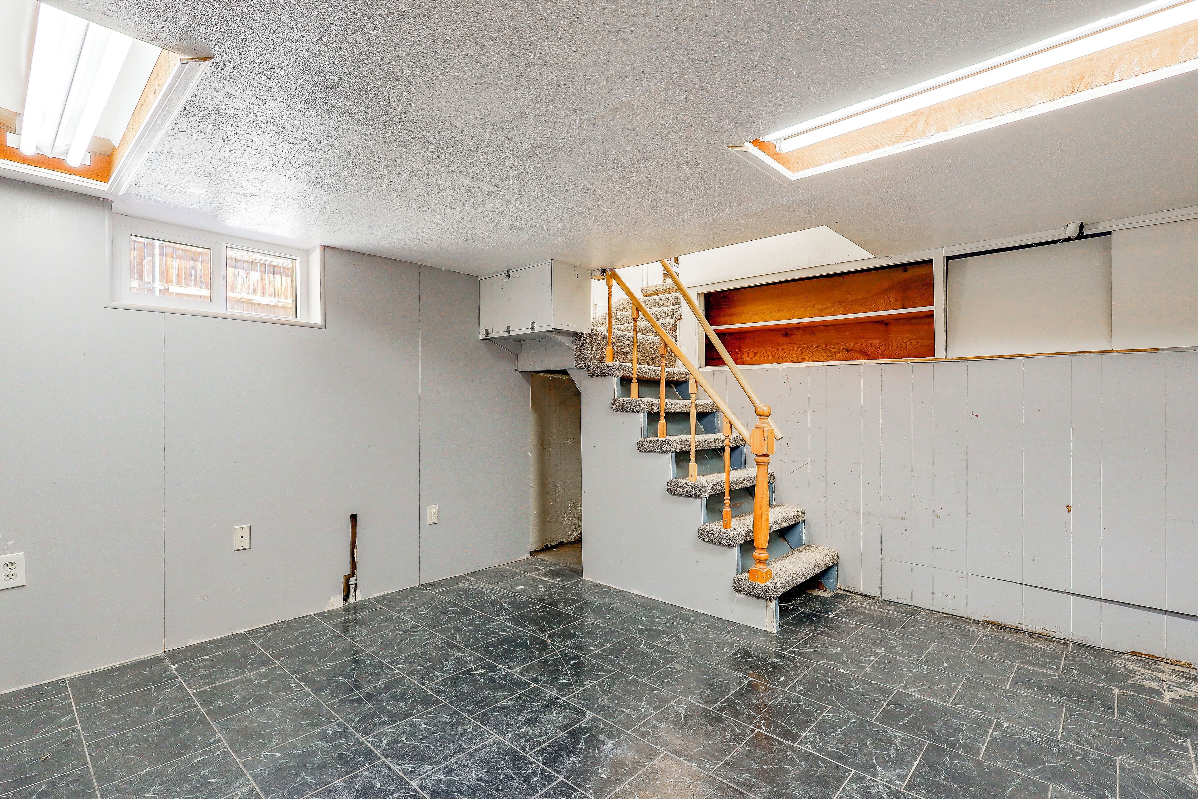 A room with a black marble floor, a wooden staircase, and a window with blinds.