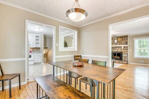 A spacious dining area with a wooden table and benches, a kitchen in the background, and a stone fireplace. - Family Getaway in Kennesaw! Spacious Home (Kennesaw)
