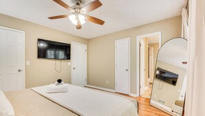 A bedroom with a bed, a ceiling fan, a flat-screen TV, and a large mirror. - Family Getaway in Kennesaw! Spacious Home (Kennesaw)