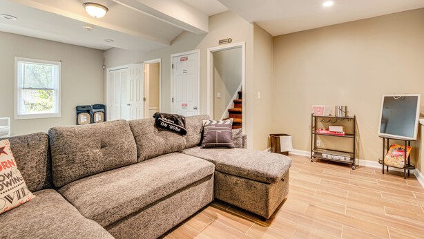 A living room with a sectional sofa, a coffee table, a TV stand with a menu board, and a staircase leading to another level. - Family Getaway in Kennesaw! Spacious Home (Kennesaw)