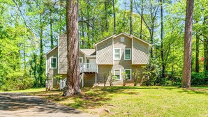 A two-story house with a front porch and a garage, surrounded by trees. - Family Getaway in Kennesaw! Spacious Home (Kennesaw)