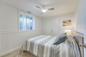 Un dormitorio con cama, ventilador de techo, ventana con persianas, puerta y lámpara en la pared.