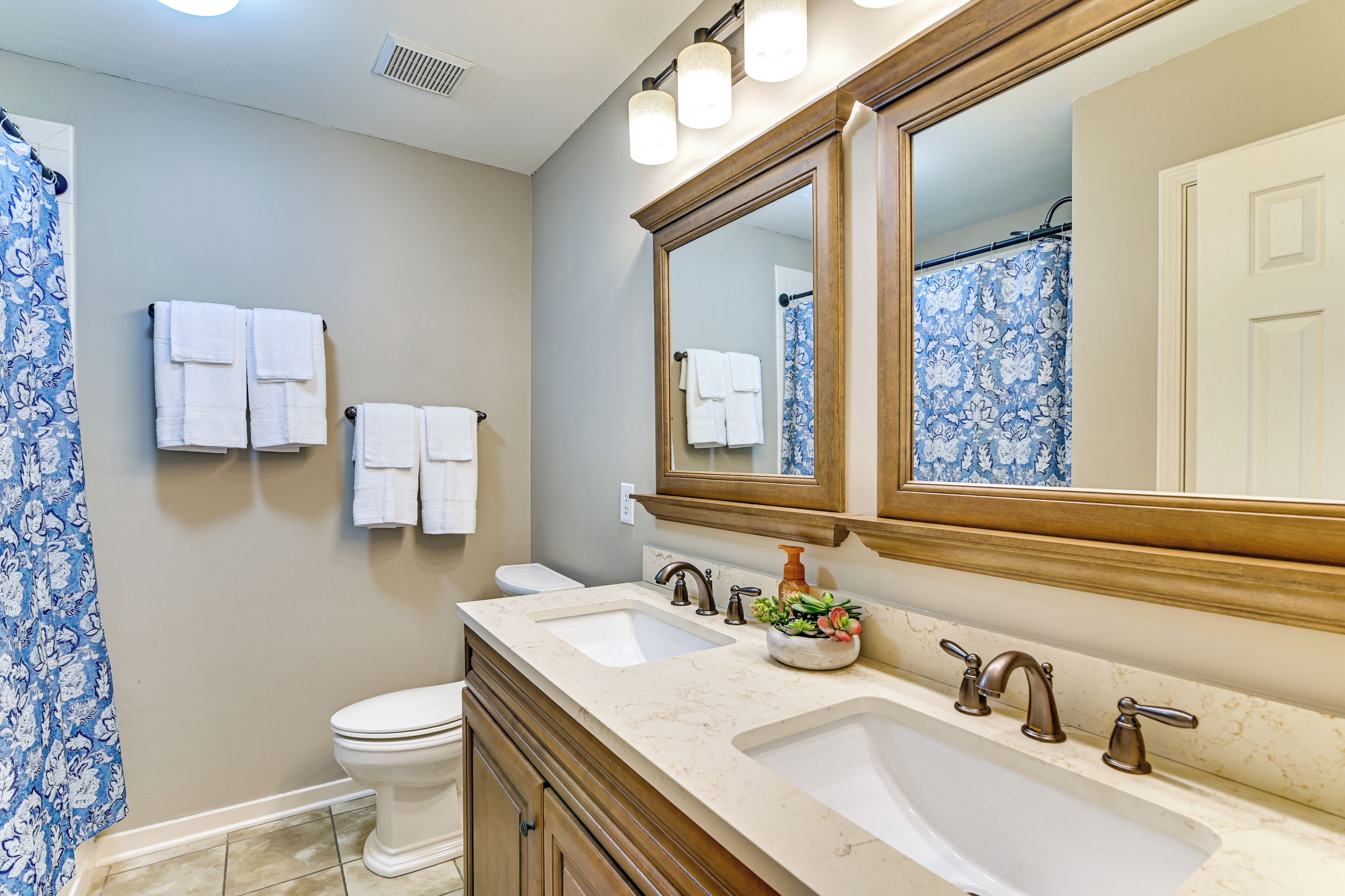 A bathroom with a double sink, a toilet, and a large mirror with lights.
