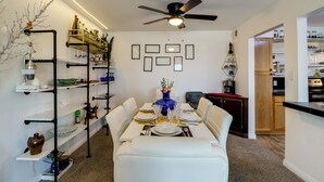 A dining area with a table set for four, surrounded by white chairs. There is a ceiling fan above and a wall-mounted shelf with various items on the left. - Walkable & Renovated Gem! Only 8 Mi to Dtwn Tucson (Tucson)