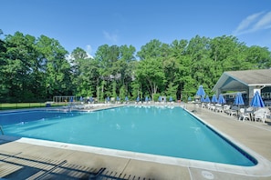 A rectangular swimming pool with a tiled deck, surrounded by white lounge chairs and blue umbrellas.