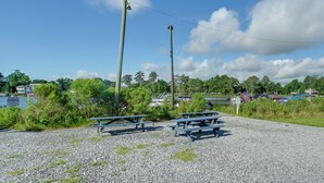 A gravel area with picnic tables, a body of water, and a boat dock in the background.