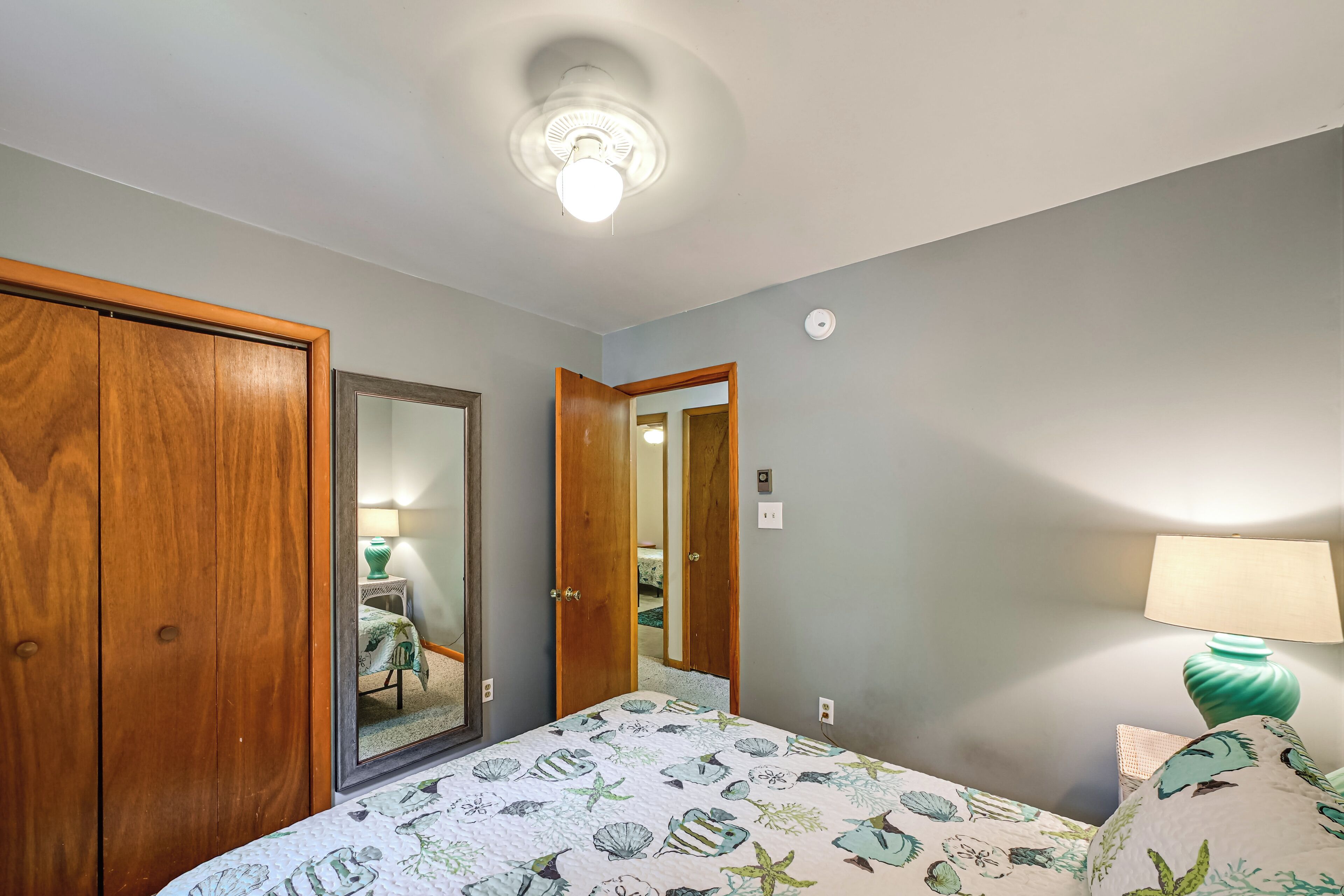 Quarto com cama, guarda-roupa de madeira, espelho, porta e luz no teto.