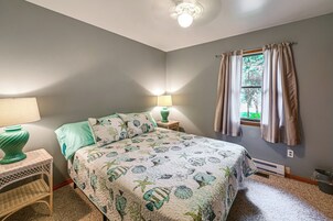 Un dormitorio con una cama, dos lámparas de noche, una ventana con cortinas y un radiador.
