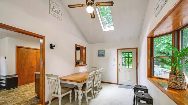 A dining area with a wooden table and chairs, a ceiling fan, and a view of greenery through the windows. - Lewes Family Escape w/ Angola by the Bay Amenities (Lewes)