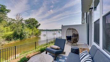A balcony with a view of a river, a wicker chair, and a sofa with cushions.