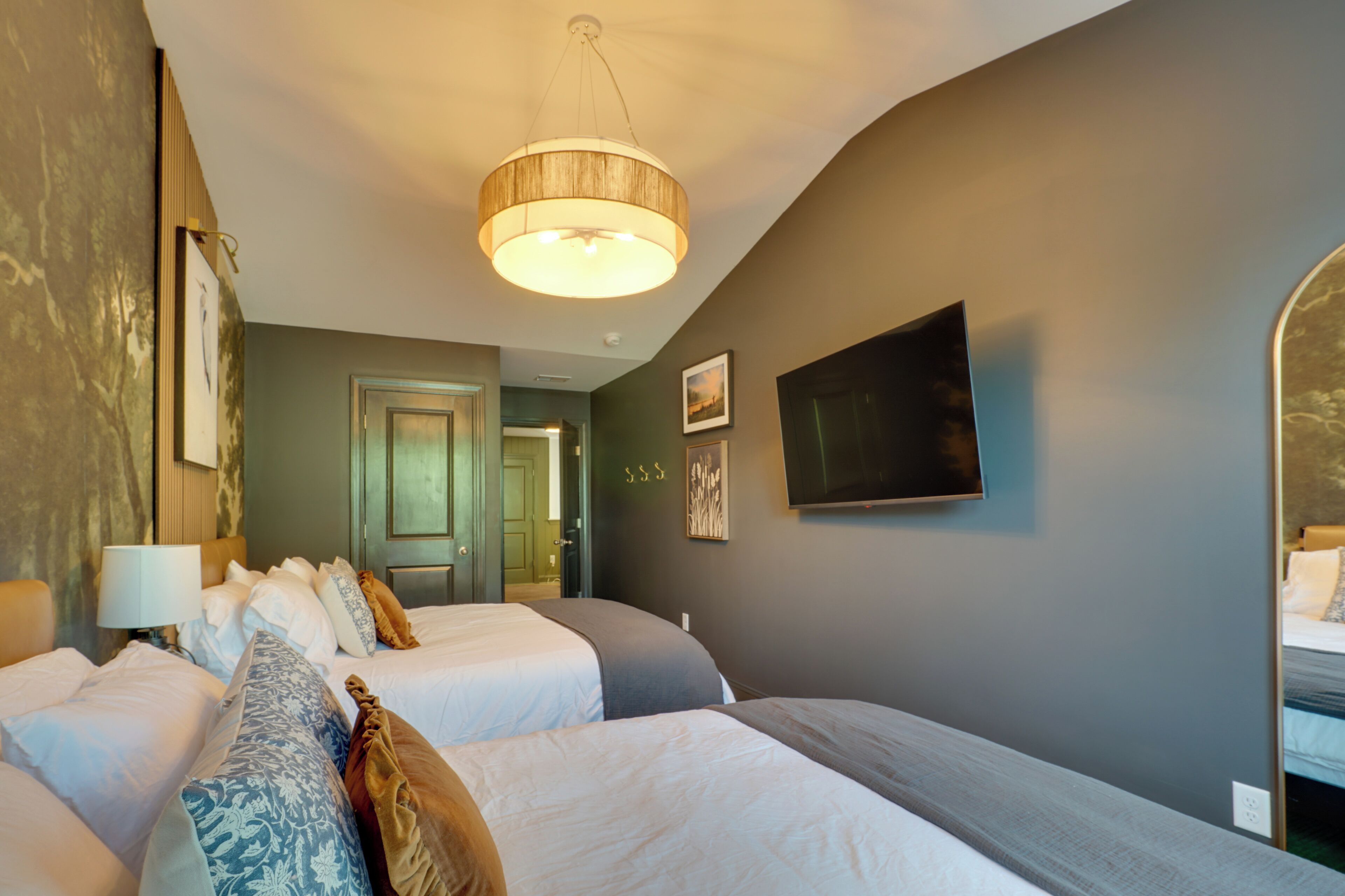 A hotel room with two beds, a television, and a mirror.