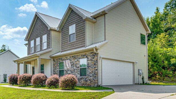 A two-story residential building with a stone facade, a garage, and a well-maintained lawn.