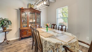 A dining room with a wooden table, chairs, a glass-top china cabinet, and a window with blinds.