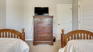 A bedroom with two wooden beds, a dresser with drawers, a television on top, and a white door.