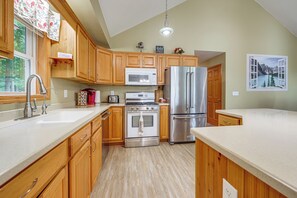 A modern kitchen with wooden cabinets, stainless steel appliances, and a view of a mountain lake through an open window. - Unplug & Unwind! Romulus Family Gem w/ Swim Pond (Romulus)