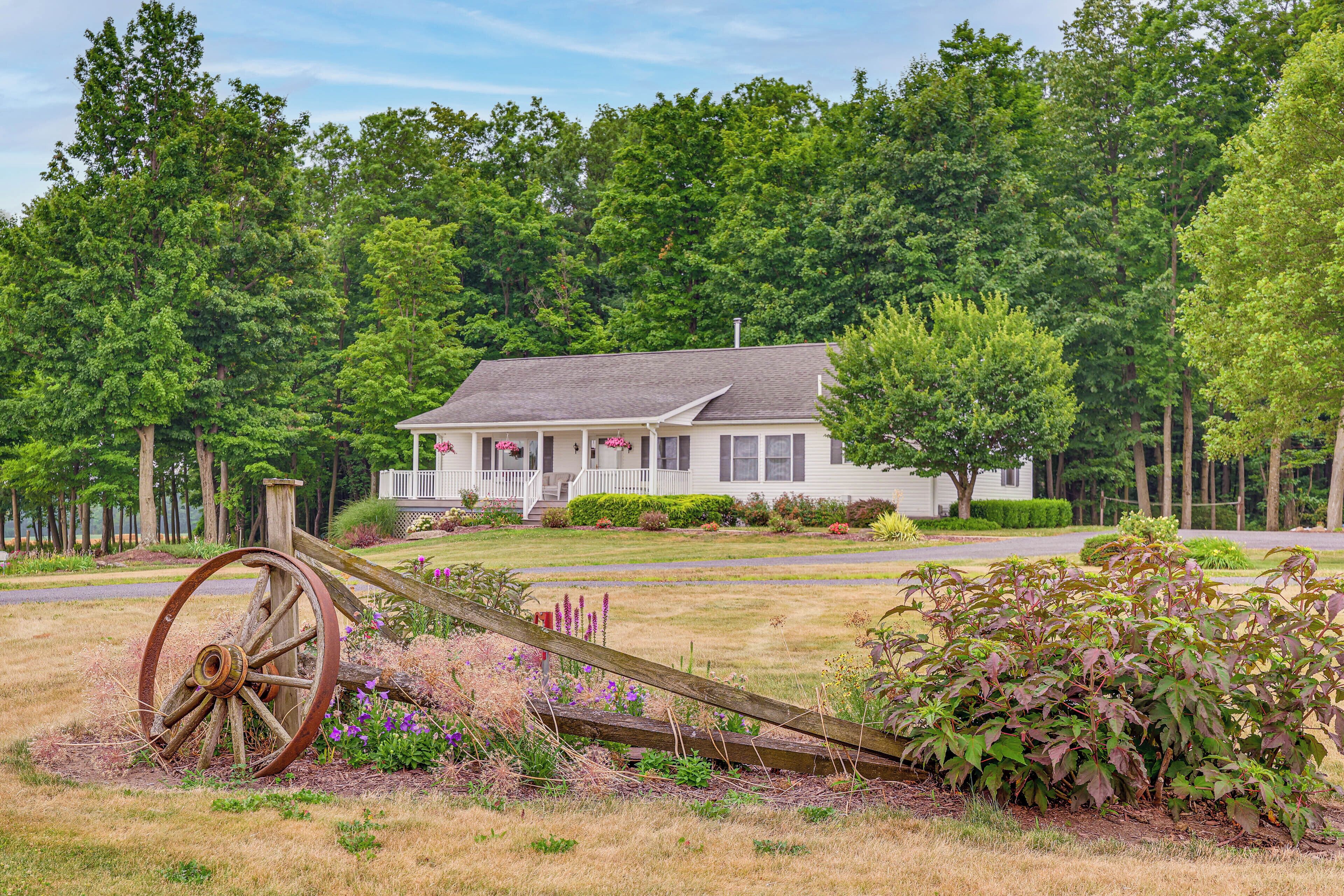 A house with a porch, surrounded by a grassy yard and a large wooden wheel.