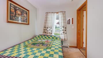 A bedroom with a bed, a window with curtains, a door, and a painting on the wall.