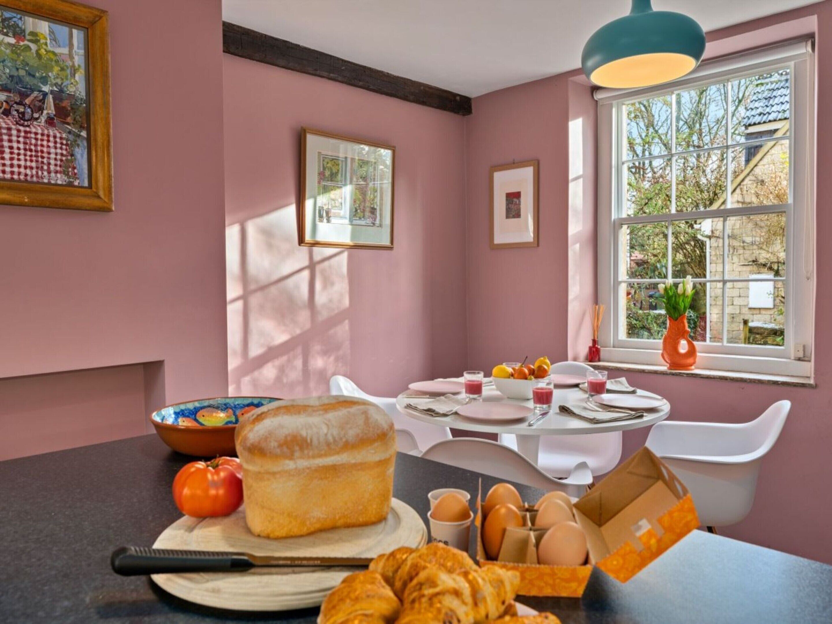 Un comedor con una mesa dispuesta para dos personas, una hogaza de pan, huevos y un croissant en la encimera.