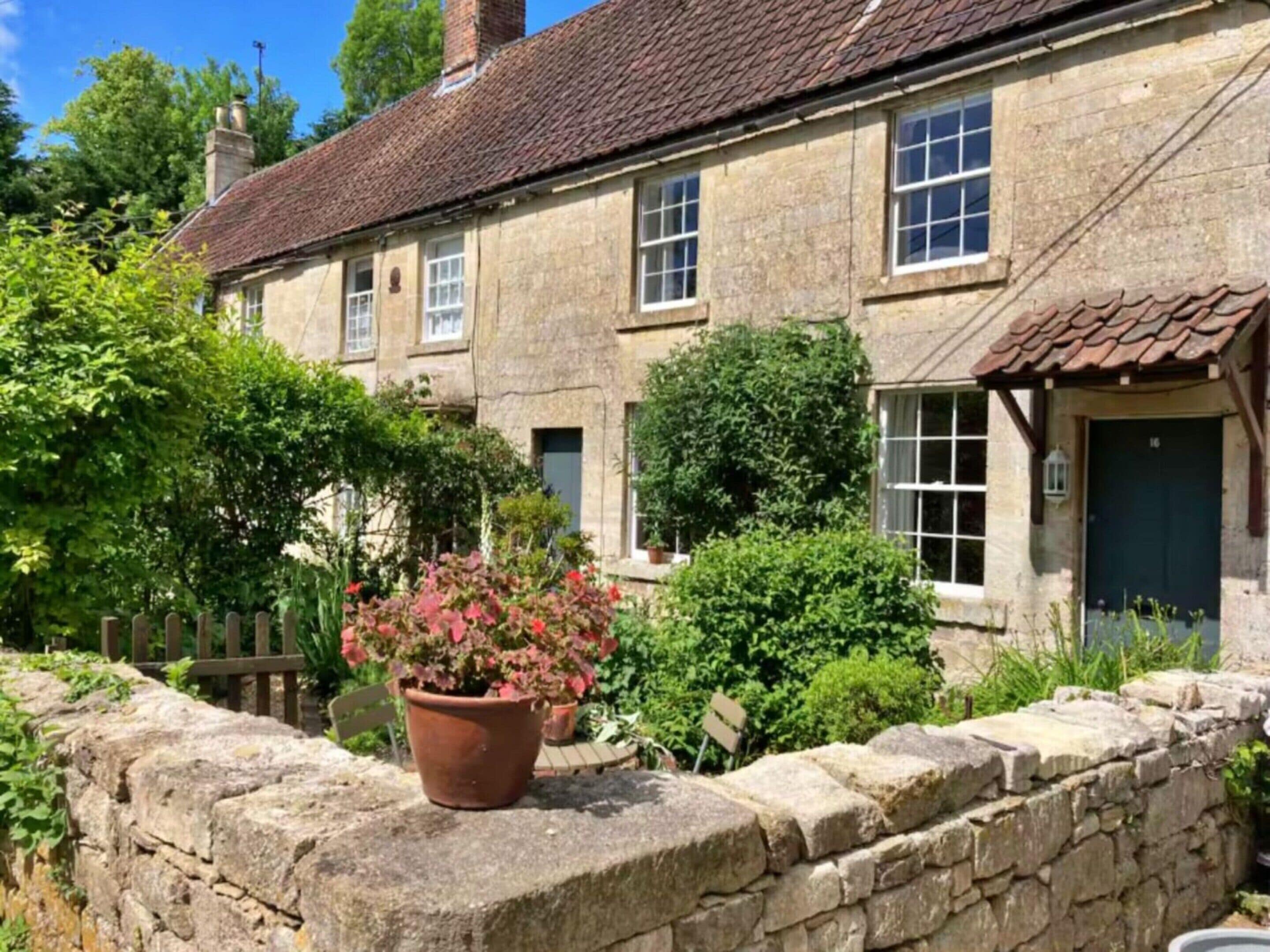 A stone house with a tiled roof, multiple windows, and a stone wall with a potted plant.