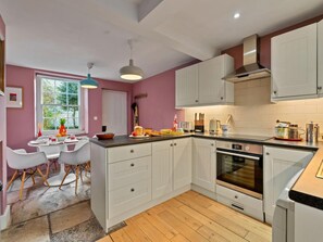A modern kitchen with white cabinetry, a central island, and a dining area with white chairs. - Historic Wiltshire Garden Cottage (Trowbridge)