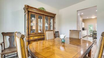 A dining room with a large wooden table surrounded by chairs, a cabinet with glass doors, and a vase with flowers.
