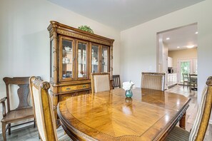 A dining room with a large wooden table surrounded by chairs, a cabinet with glass doors, and a vase with flowers.