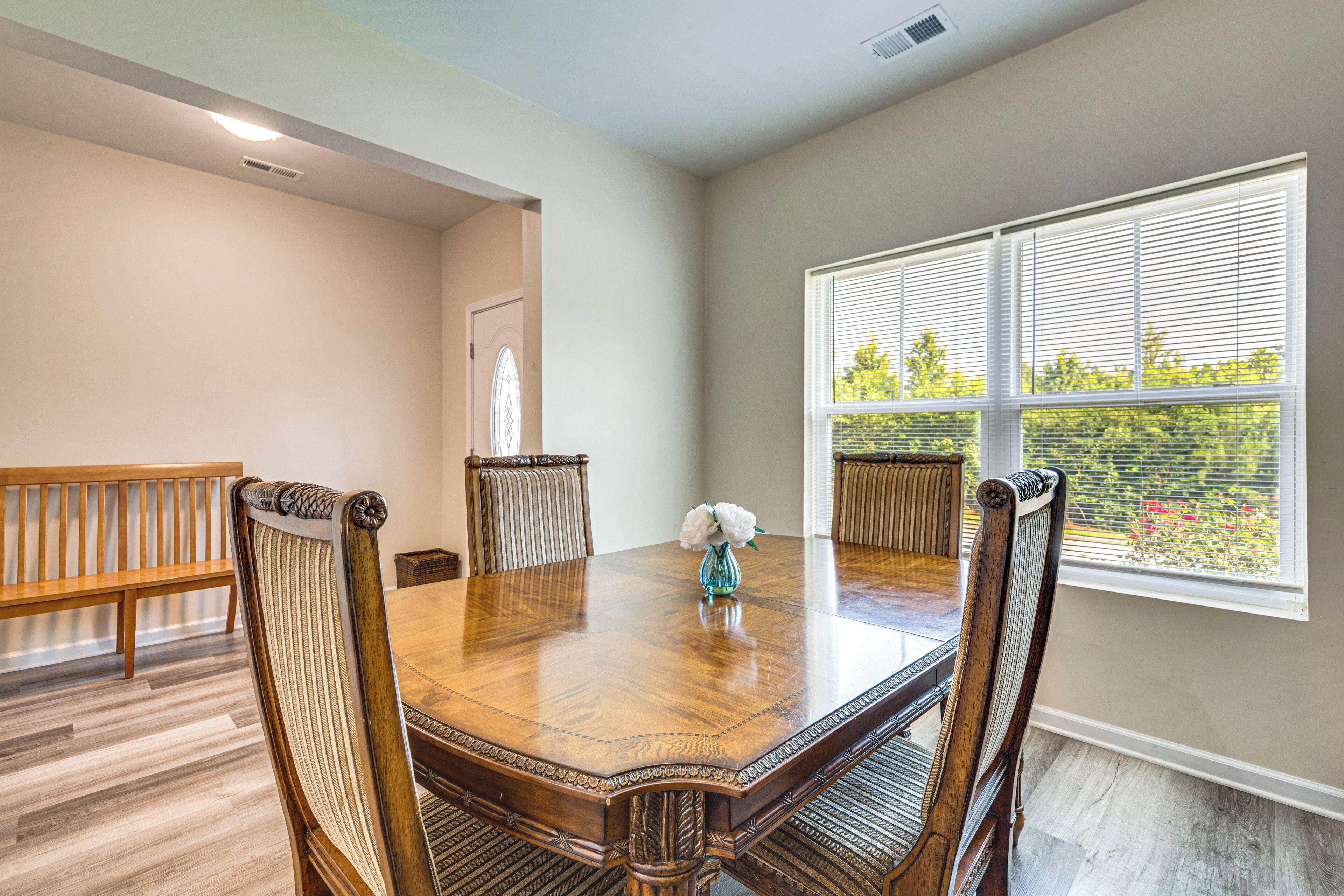 A dining room with a wooden table, four chairs, and a window with blinds.