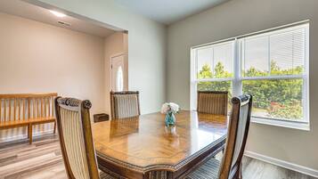 A dining room with a wooden table, four chairs, and a window with blinds.