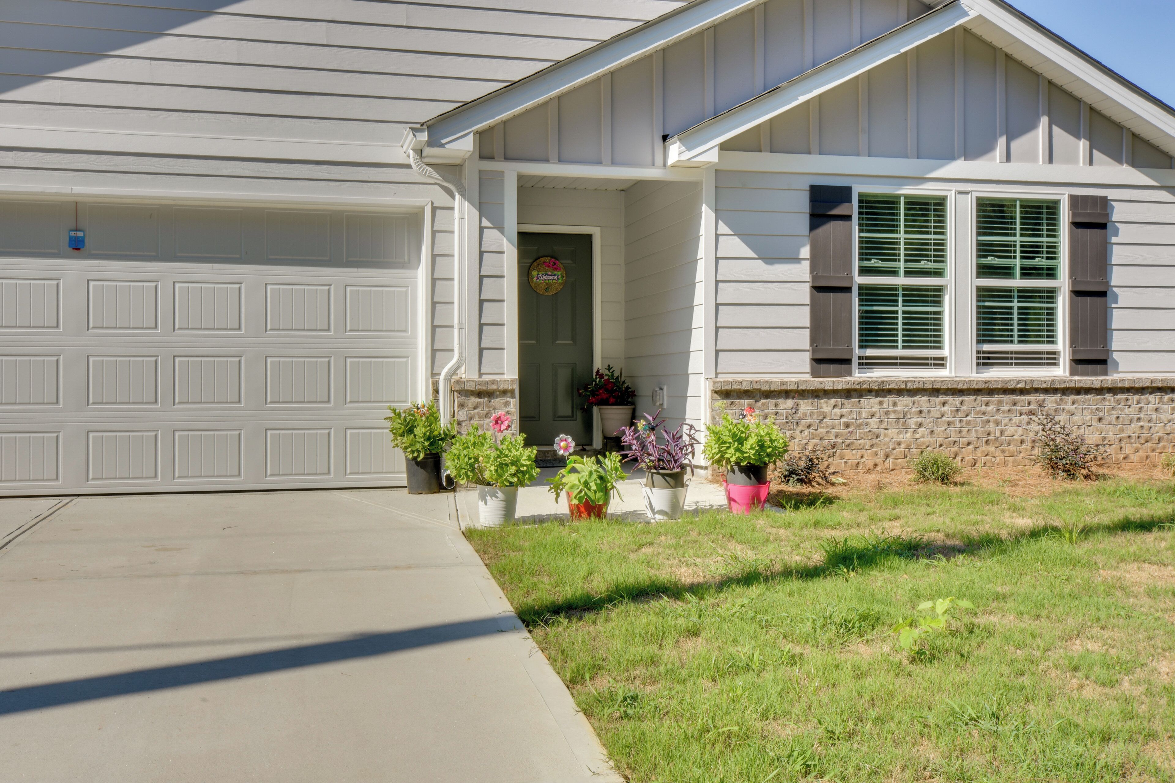A residential house with a garage, a front porch with potted plants, and a brick foundation.