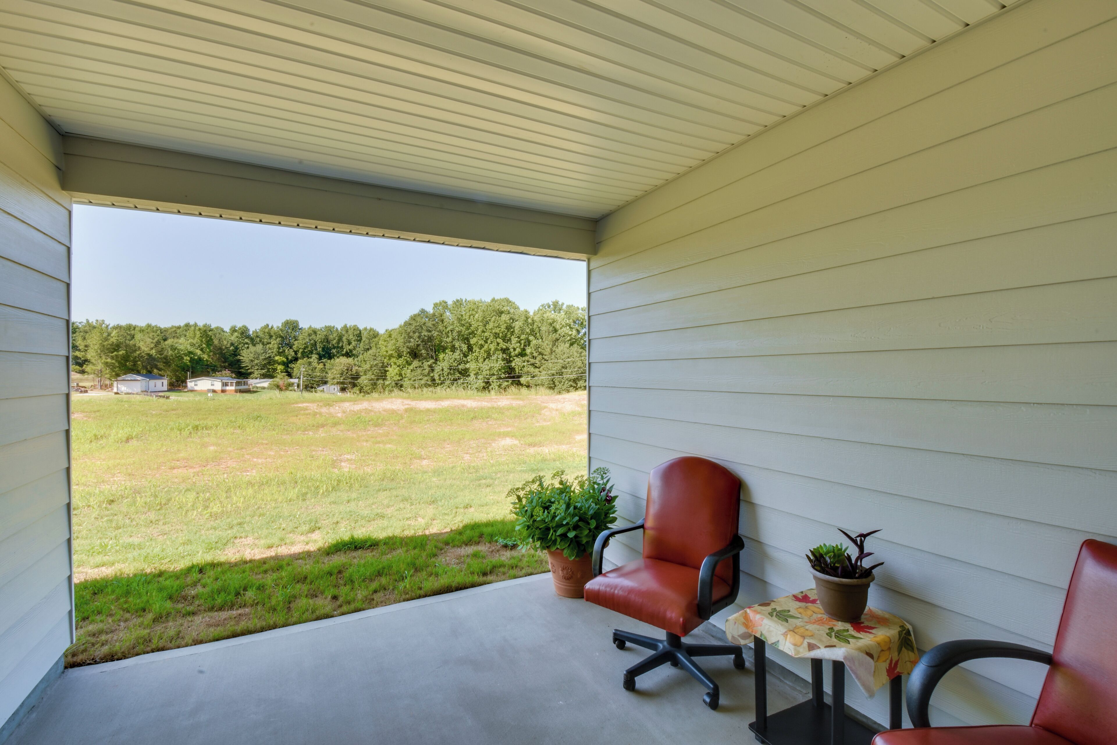 A covered porch with two chairs, a small table, and potted plants.