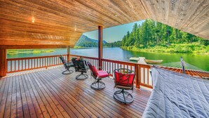 Un terrazzo in legno con posti a sedere all'aperto, vista su un lago e un paesaggio boschivo.