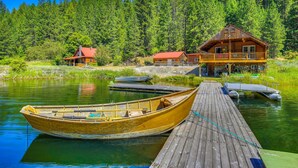 Una baita di legno con un molo che si protende in un lago calmo, circondata da una fitta foresta.