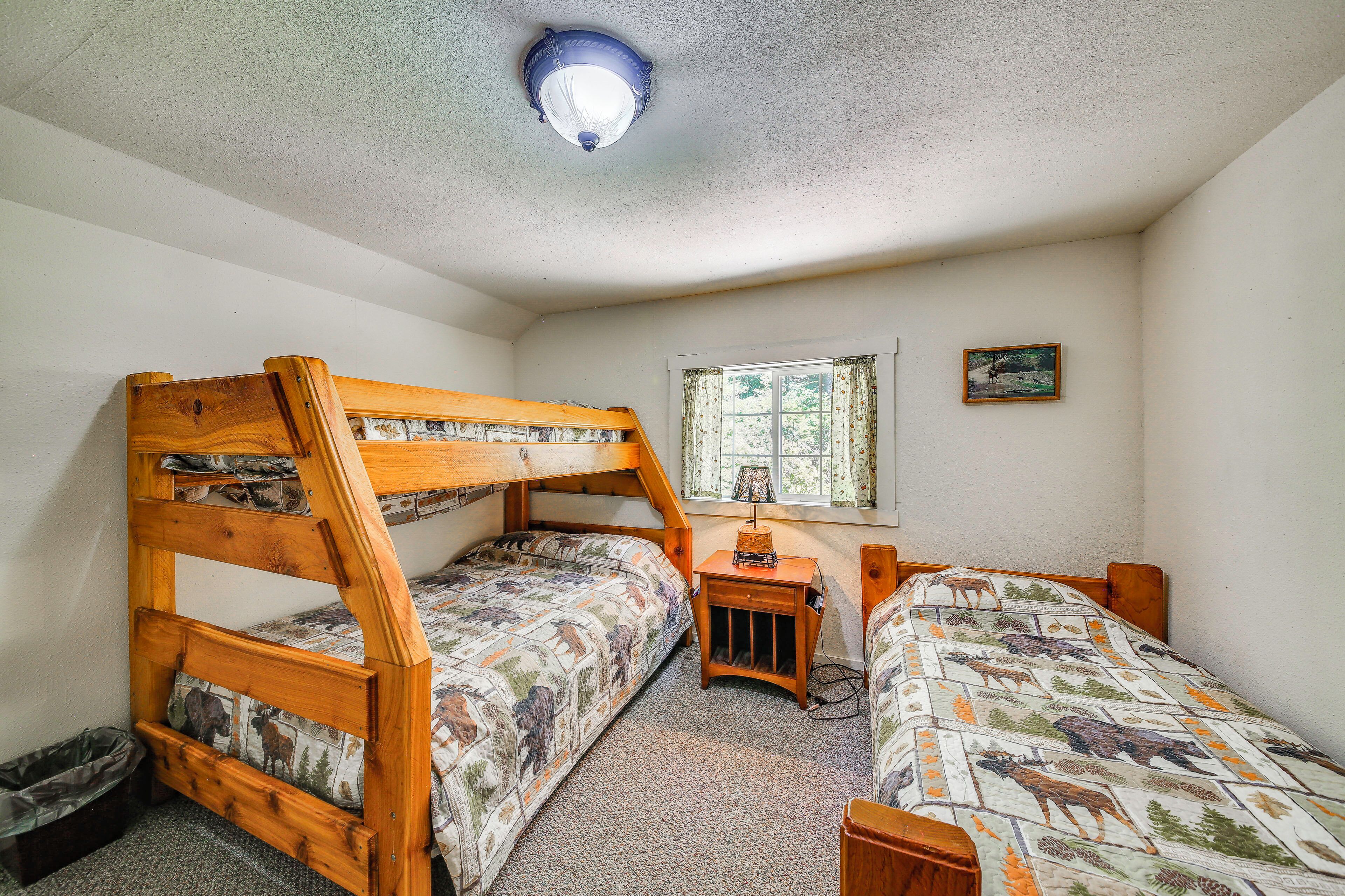 A room with bunk beds, a small table, a window with curtains, and a ceiling light fixture.