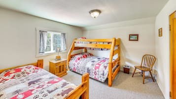 A bedroom with two bunk beds, a window with curtains, a small wooden cabinet, a chair, and a framed picture on the wall.