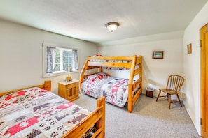A bedroom with two bunk beds, a window with curtains, a small wooden cabinet, a chair, and a framed picture on the wall. - 700-acre Property w/ 33-acre Lake & Dual Cabins! (Chewelah)