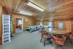 A cozy cabin interior with a wooden ceiling, a dining table with chairs, a sofa, and a small kitchen area.