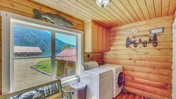 Interior de una cabaña con un ventanal grande, lavadora y un banco.