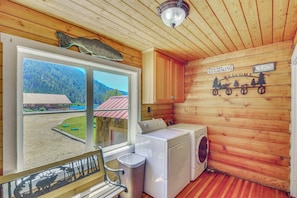 Interior de una cabaña con un ventanal grande, lavadora y un banco.
