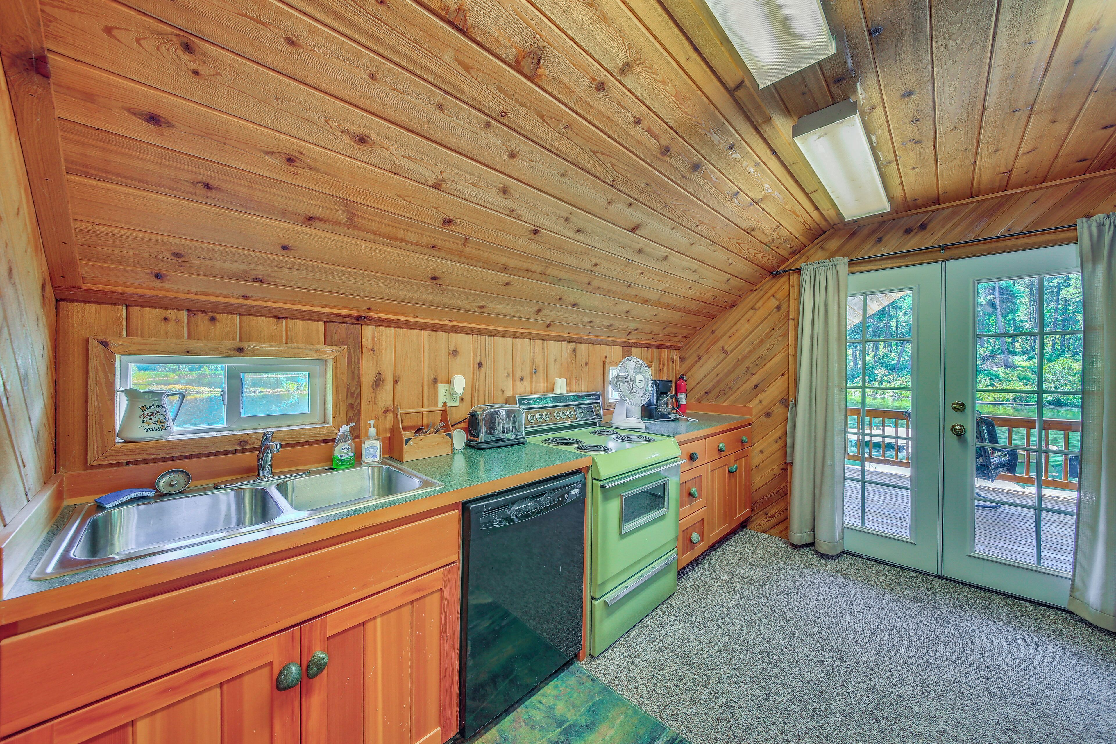 Cocina de cabaña de madera con un lavamanos, estufa y vistas al exterior por una puerta.
