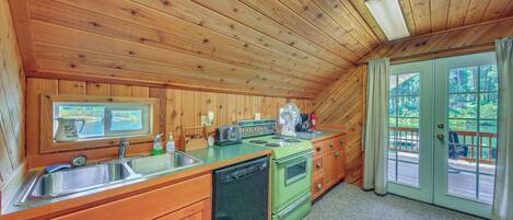 Cocina de cabaña de madera con un lavamanos, estufa y vistas al exterior por una puerta.