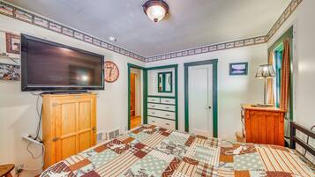 A bedroom with a large flat-screen TV, a wooden cabinet, a quilted bedspread, and a wall clock.