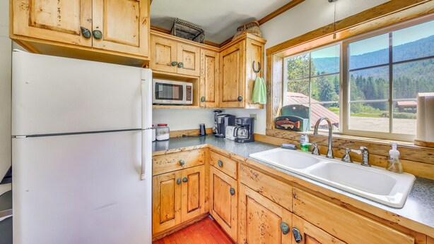 Una cucina con mobili in legno, un frigorifero, un forno a microonde, una macchina da caffè e una finestra vista montagne.