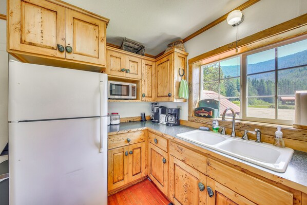A kitchen with wooden cabinets, a refrigerator, a microwave, a coffee maker, and a window with a view of mountains.